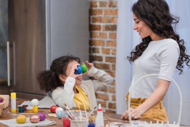 Eğleniyor ve boyalı Paskalya yumurtaları gözlerle kapsayan Afro-Amerikan kızı