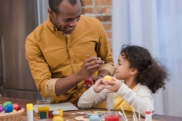 african american father painting daughter nose while painting easter eggs
