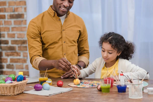 cropped image of african american father and daughter painting easter eggs