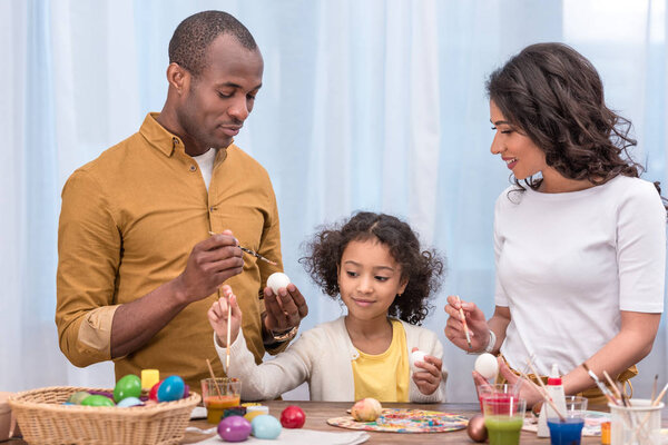 african american parents and daughter painting chicken easter eggs