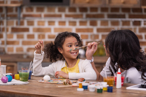 african american mother painting daughter face, easter concept
