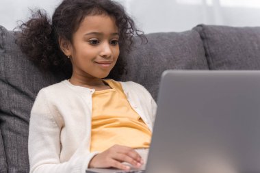 Afro-Amerikan çocuk evde kanepede dizüstü bilgisayar kullanarak