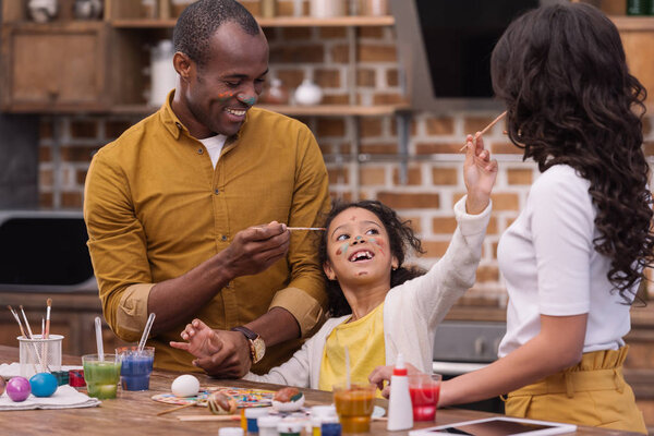 happy african american parents and daughter having fun while painting easter eggs  