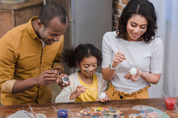 happy african american parents and daughter painting easter eggs