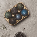 Vista superior de huevos de Pascua pintados en bandeja dorada con pintura y pincel sobre hormigón