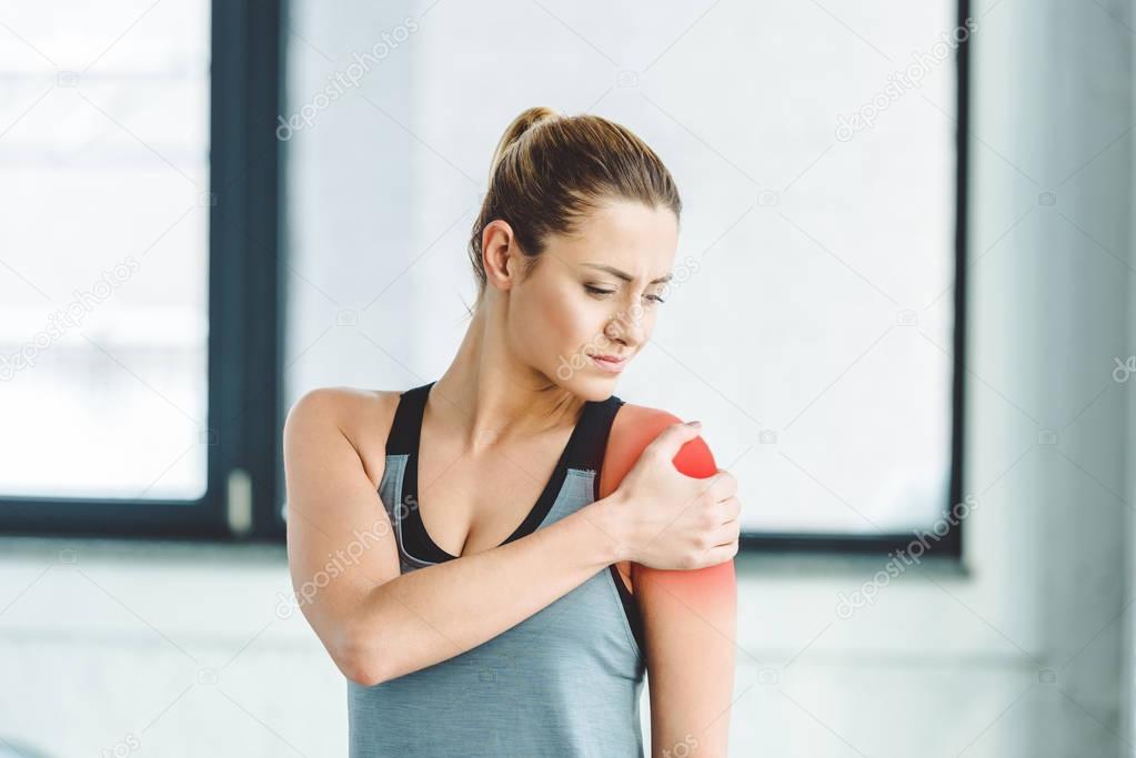 portrait of young sportswoman suffering from pain in arm at gym 