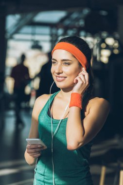 akıllı telefon ve kulaklık spor salonunda kullanan gülümseyen kadın 