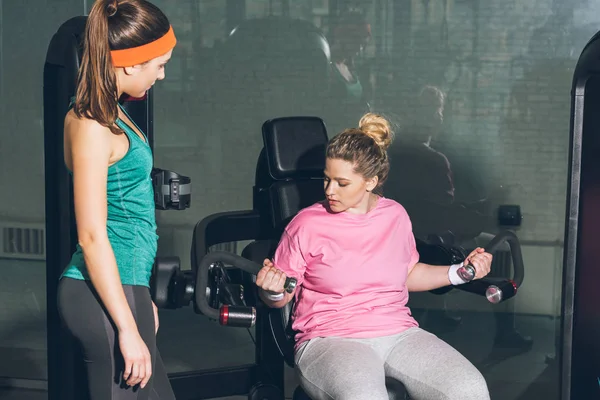 Übergewichtige Frau Trainiert Trainingsgeräten Während Der Trainer Sie Beobachtet — Stockfoto