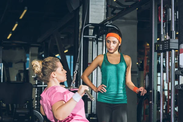 Mujer Con Sobrepeso Haciendo Ejercicio Aparato Entrenamiento Mientras Entrenador Observa —  Fotos de Stock