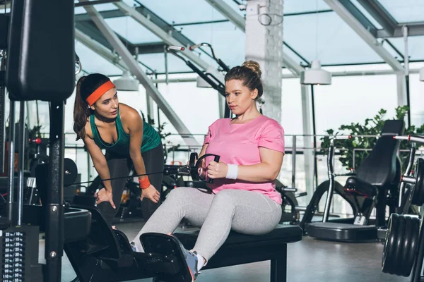 Mujer Con Sobrepeso Haciendo Ejercicio Aparato Entrenamiento Mientras Entrenador Observa — Foto de Stock