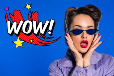 portrait of stylish woman in retro clothing and sunglasses with comic style wow sign isolated on blue clipart