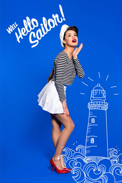 beautiful young woman in sailor shirt with lighthouse drawing and well hello sailor inscription isolated on blue