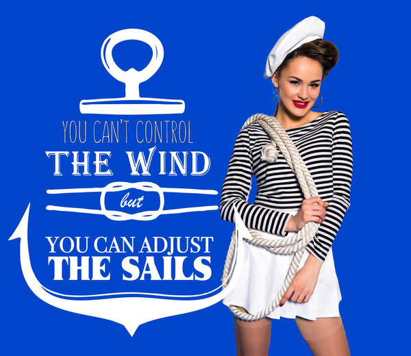smiling beautiful young woman in sailor shirt with rope and motivational inscription isolated on blue