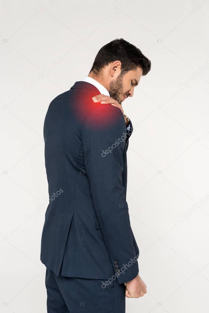 back view of young businessman suffering from ache in shoulder isolated on grey