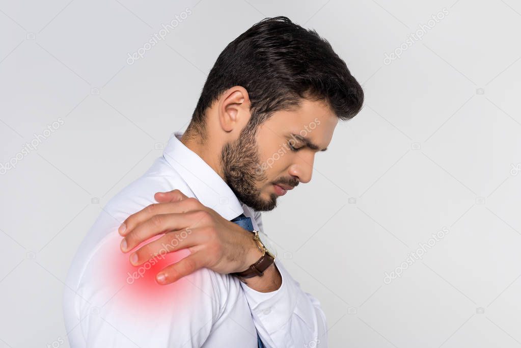 young overworked businessman suffering from pain in shoulder isolated on grey 