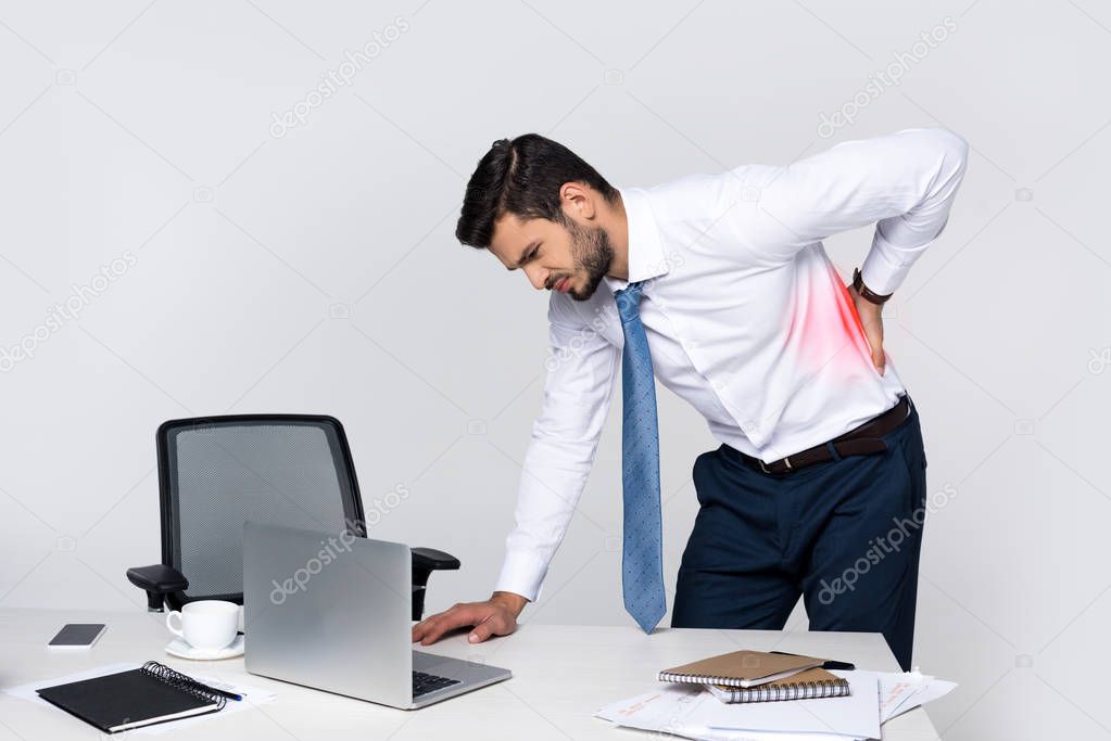 young businessman suffering from backache while leaning at table with laptop