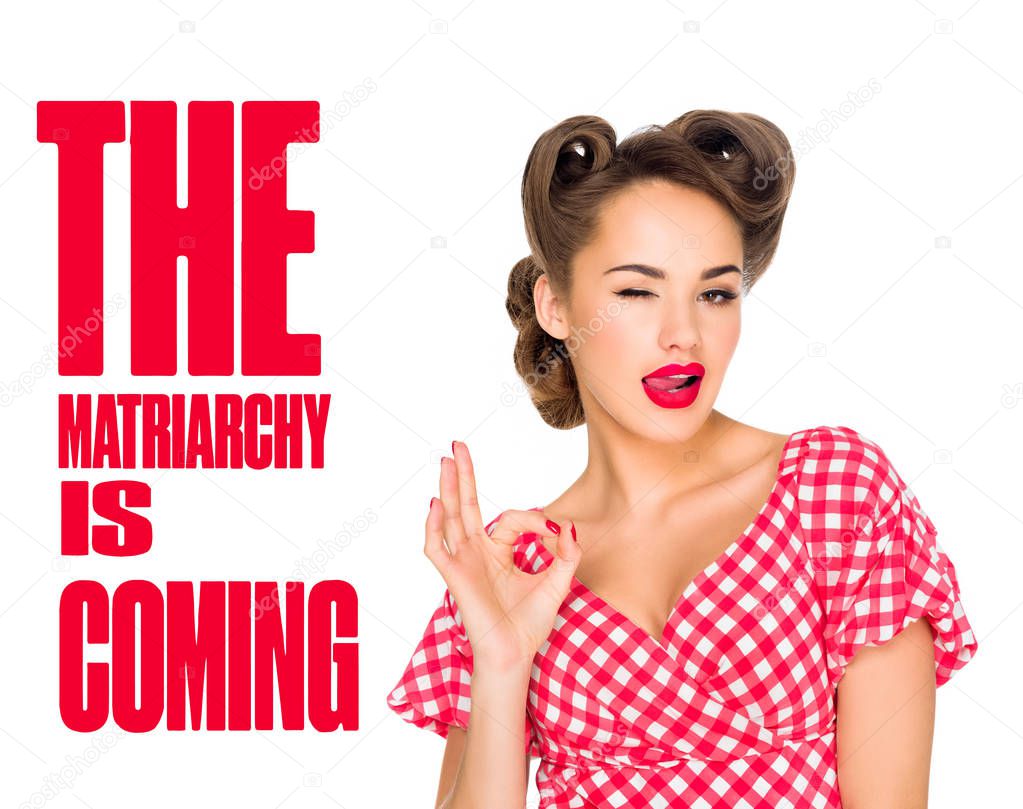 beautiful woman in retro clothing sticking tongue out and showing ok sign with matriarchy is coming lettering isolated on white
