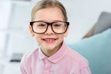 evde kameraya bakarak gözlük gülümseyen çocuk portresi