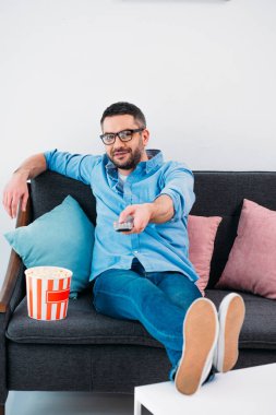 man in eyeglasses resting on sofa and watching tv at home clipart