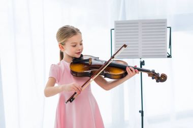 smiling little child in pink dress playing violin at home clipart