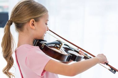 side view of cute little child in pink dress playing violin at home clipart