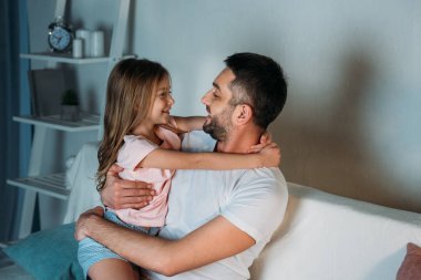 Baba ve kızı evde birbirine bakarak gülen in yan görünüm