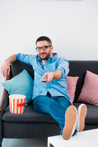 man in eyeglasses resting on sofa and watching tv at home