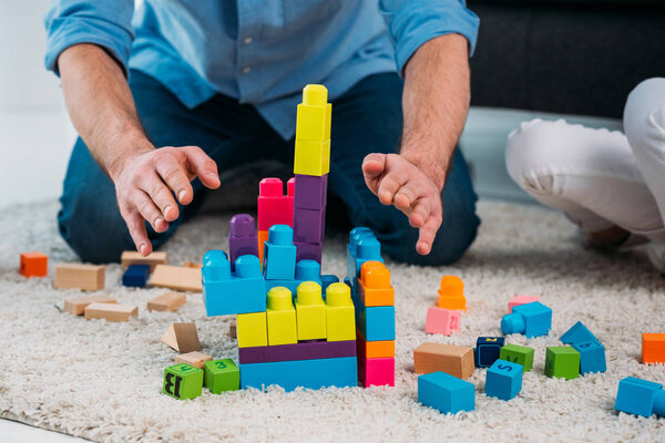 part view of kid and father playing with colorful blocks together on floor at home
