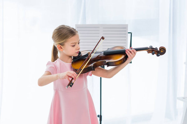 cute little child in pink dress playing violin at home