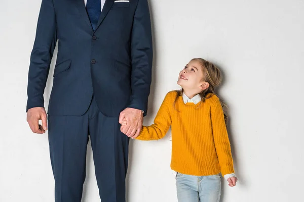 悲しい娘とグレーに分離された手を繋いでいるビジネス スーツで父親の部分的なビュー — ストック写真