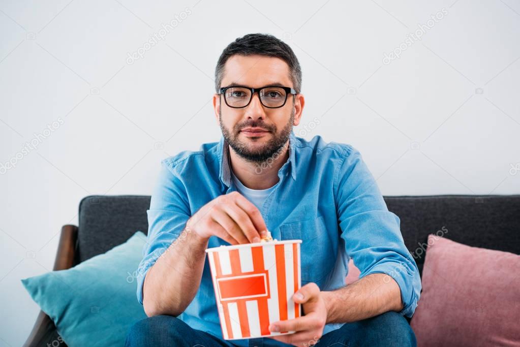 portrait of man in eyeglasses with popcorn watching tv