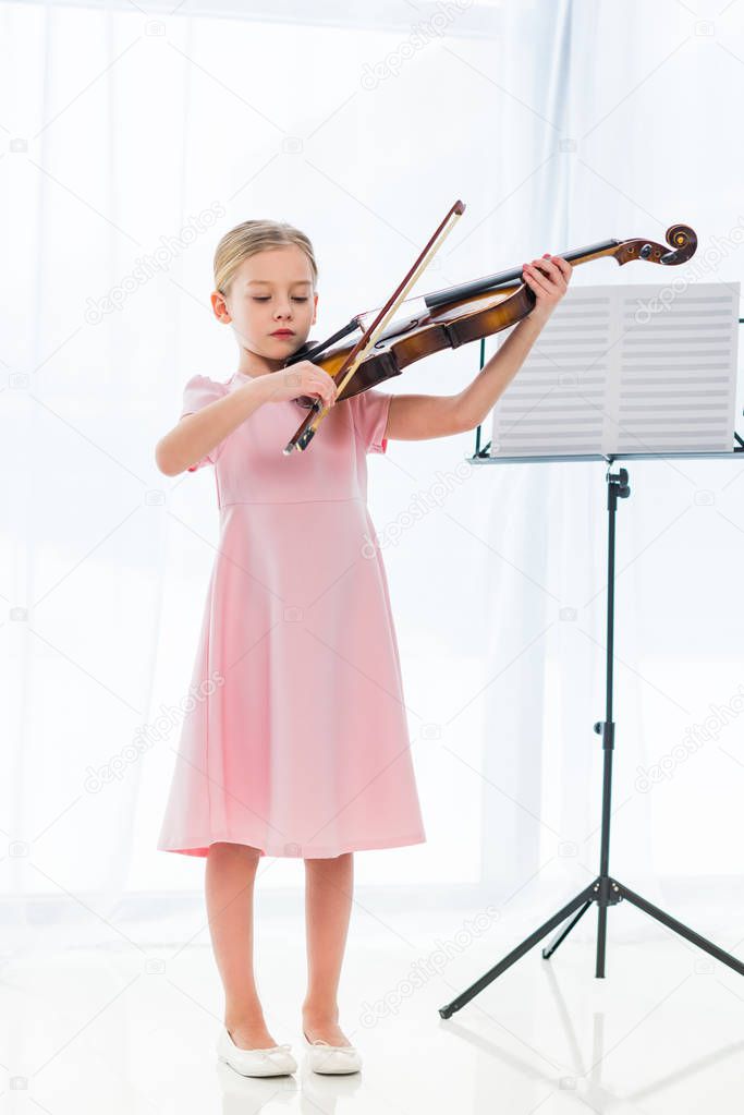 cute little child in pink dress playing violin at home