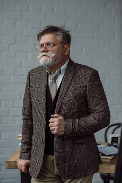 senior writer in tweed suit and eyeglasses near workplace