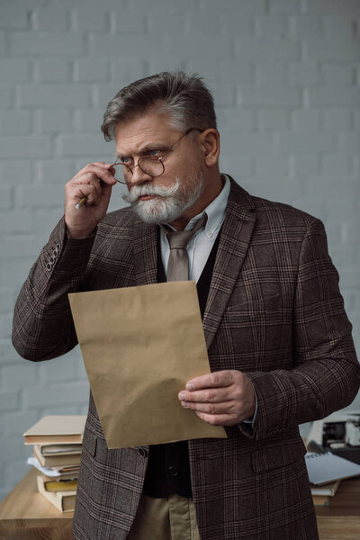 senior writer in tweed suit and eyeglasses with letter near workplace