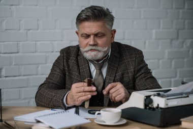senior writer looking at watch while sitting at workplace clipart