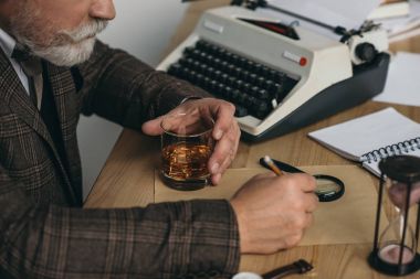 el yazması üzerinde çalışma ve bardak viski tutan kıdemli yazar kırpılmış atış