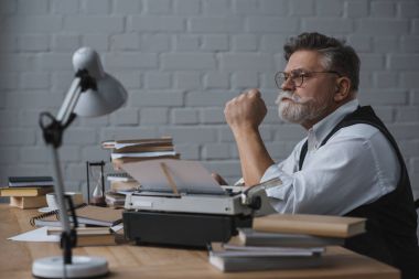thoughtful senior writer sitting at workplace and looking away clipart