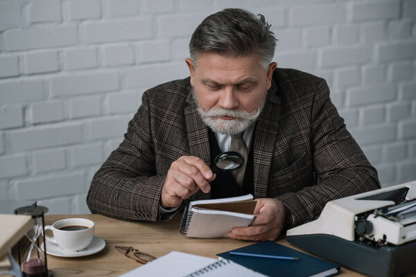 handsome senior writer reading manuscript with magnifying glass