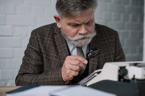 bearded senior writer reading manuscript with magnifying glass
