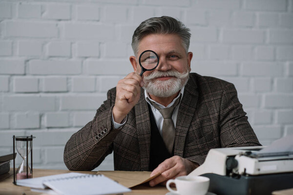 senior writer looking at camera through magnifying glass