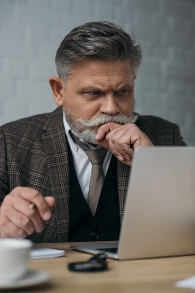 thoughtful senior man looking at laptop