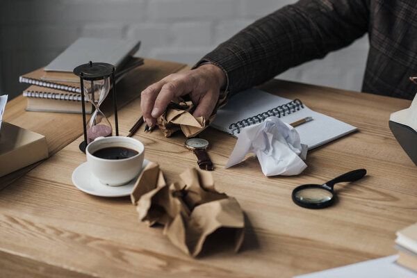 cropped shot of writer crumpling paper at messy workplace
