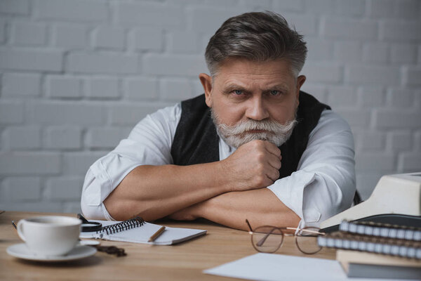 bearded senior writer sitting at workplace and looking at camera