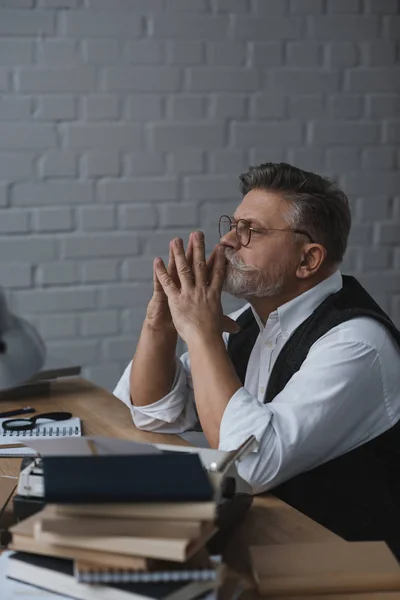 Doordachte Senior Man Zit Bij Bureau Met Stapels Boeken — Stockfoto