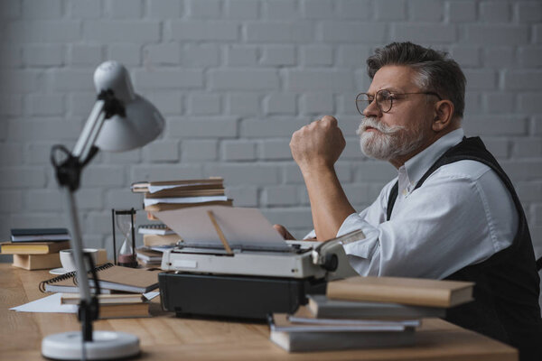 thoughtful senior writer sitting at workplace and looking away