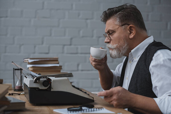 senior writer working with vintage typewriter and drinking coffee