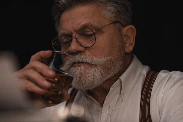 close-up portrait of senior man drinking whiskey on black