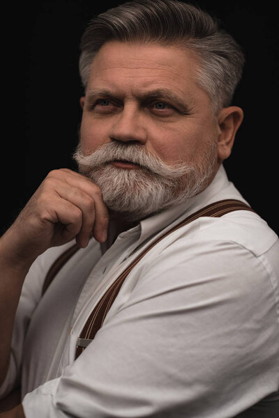 thoughtful senior man in white shirt with suspenders isolated on black