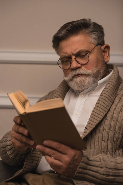 concentrated senior man in eyeglasses reading book