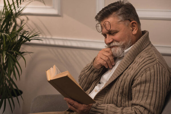 happy senior man in sweater reading book